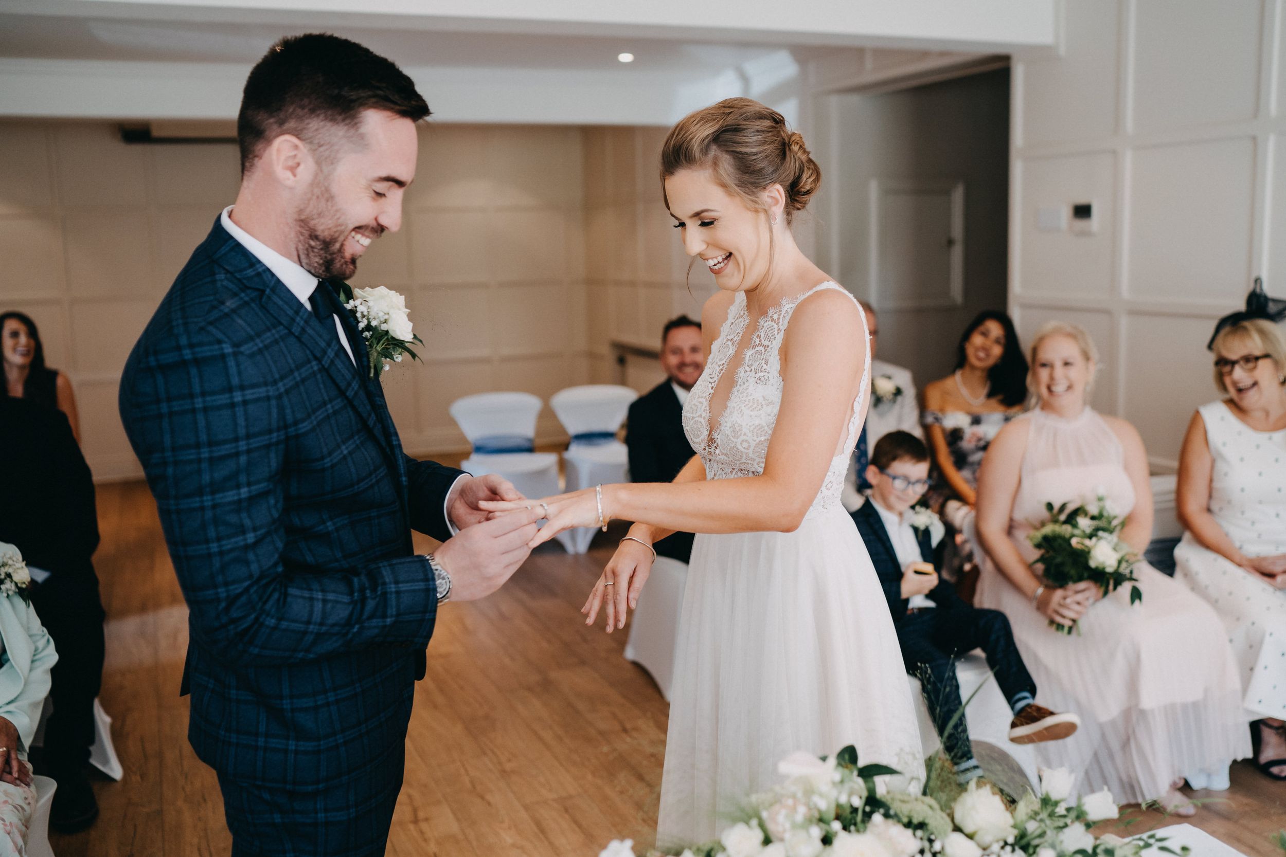 Couple exchanging rings during indoor wedding ceremony in front of seated guests.