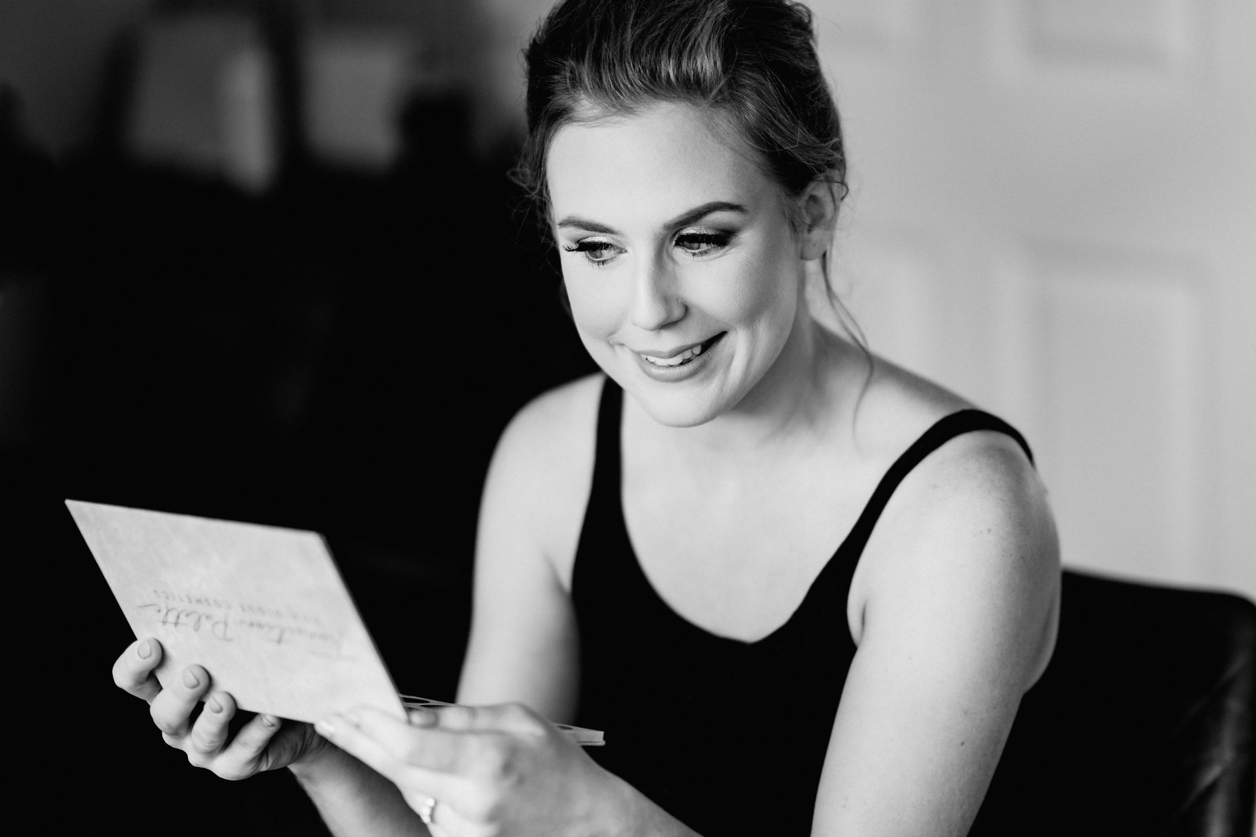 Black and white portrait of someone sitting at a table and smiling while reading a paper or document.
