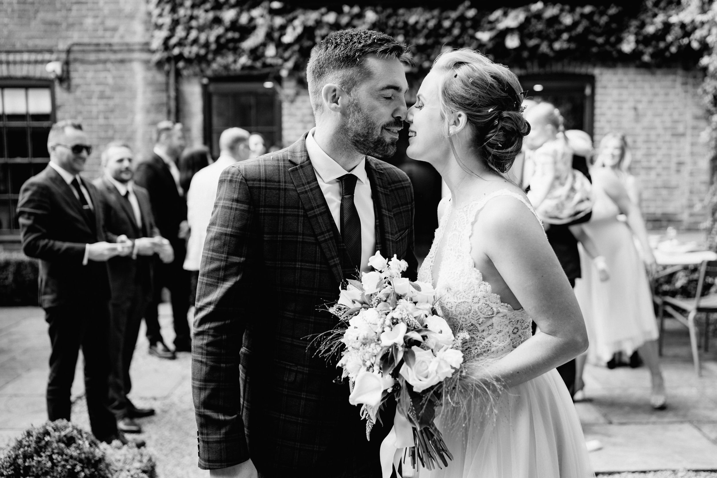 A romantic black and white photo of a couple on their wedding day with guests in the background.
