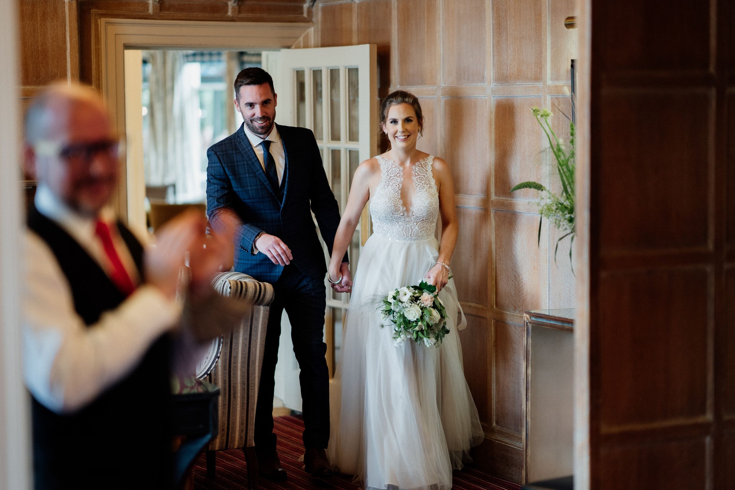 Wedding couple stands in a hallway entrance while someone in foreground gestures toward them.