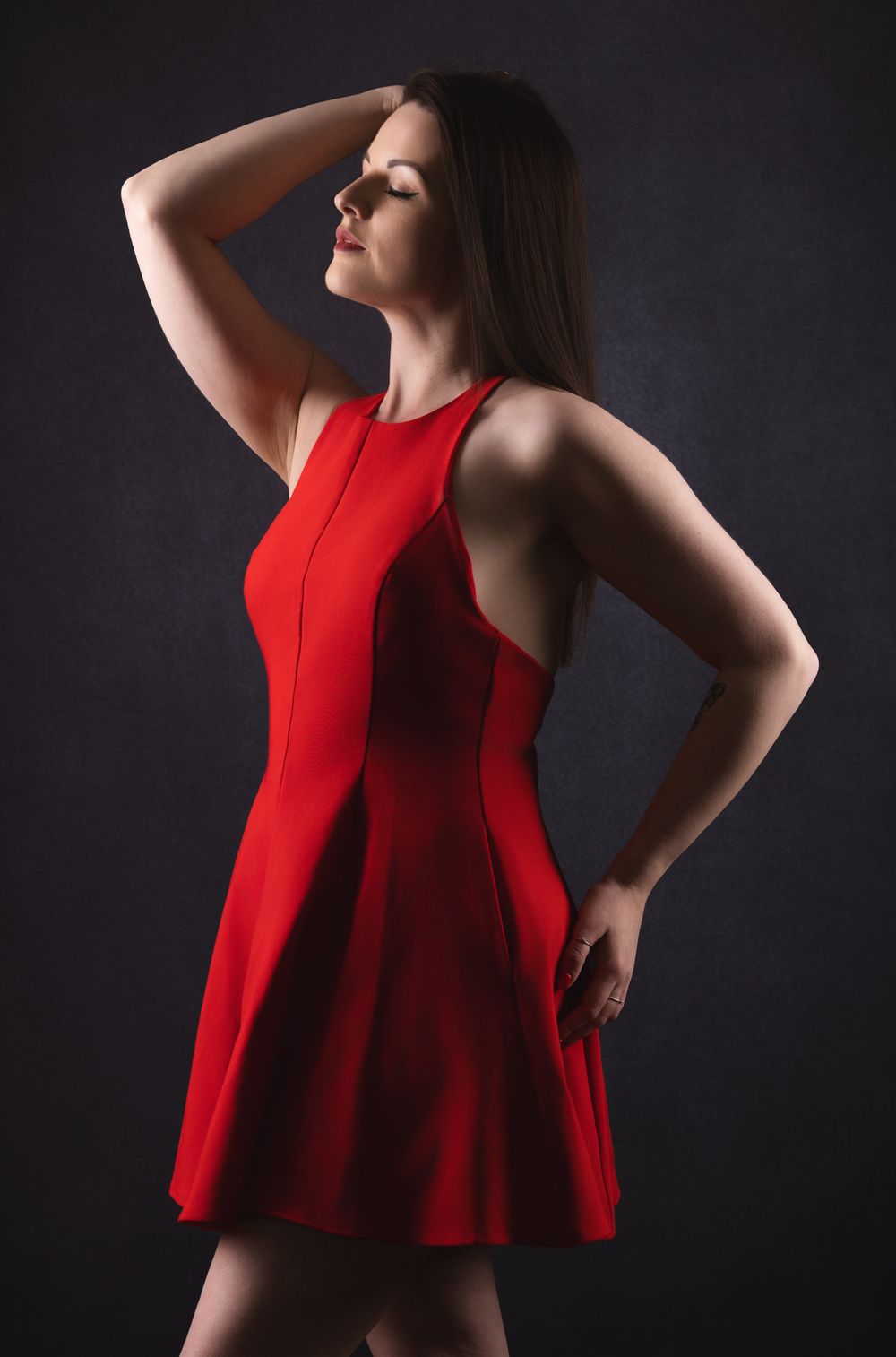 Dramatic studio portrait of a model in a red sleeveless dress striking an elegant pose against a dark background.