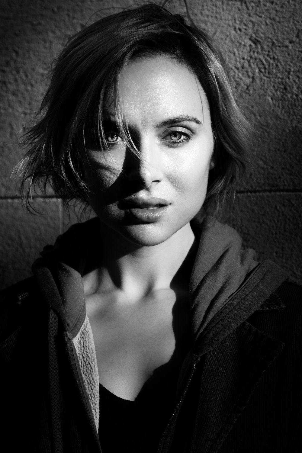 Dramatic black and white portrait with strong shadows and contrast against textured wall.