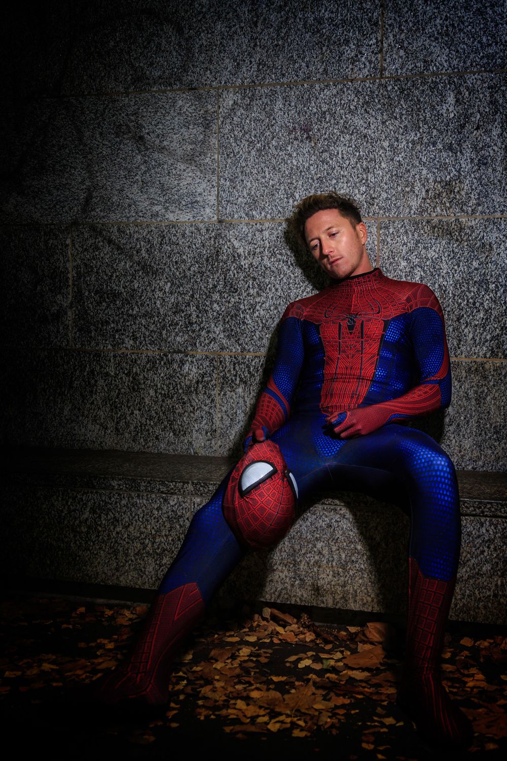 A Spider-Man cosplayer poses against a textured wall background in dramatic lighting.