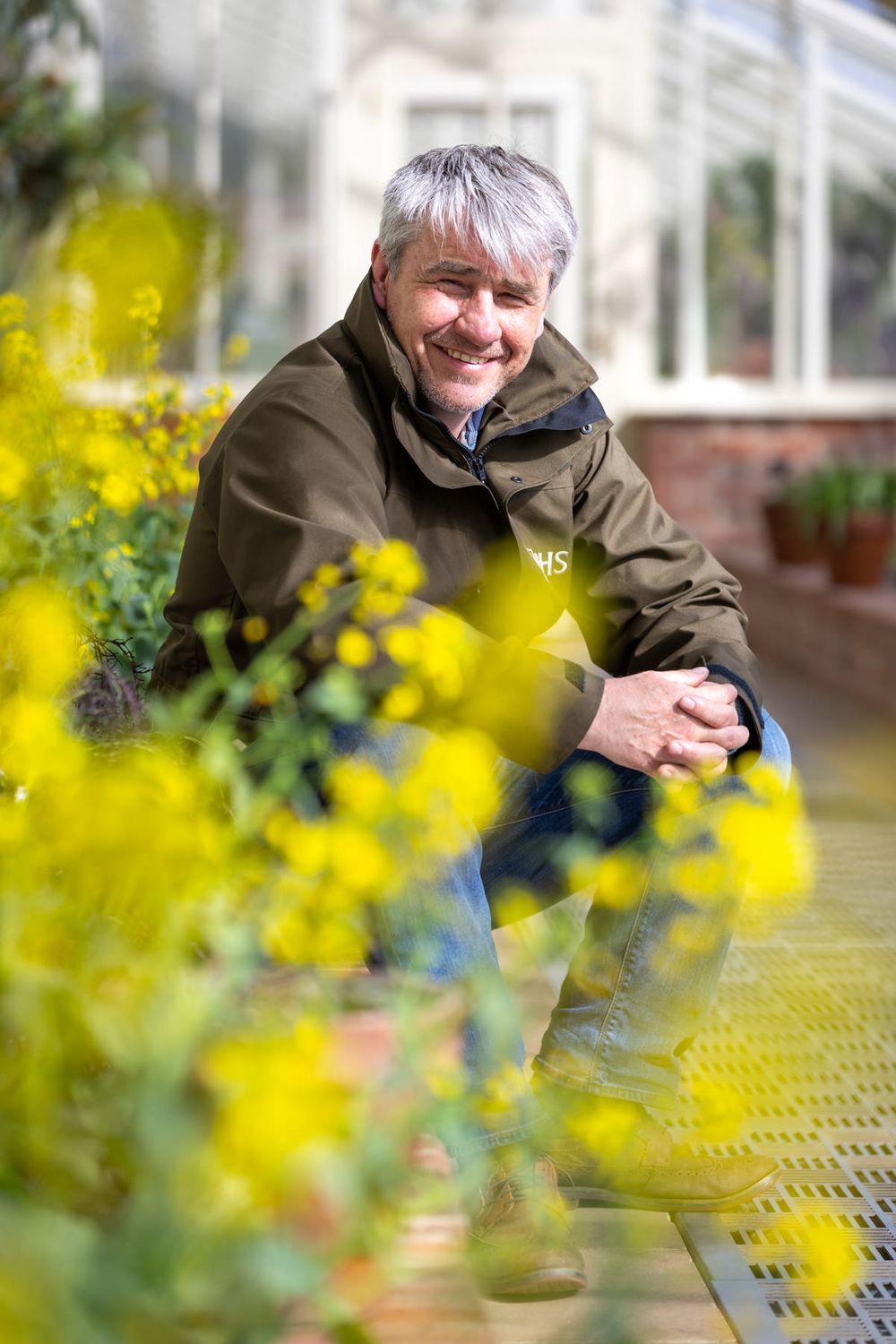 A series of five photos shows someone smiling and posing through decorative yellow flowers in front of a greenhouse.