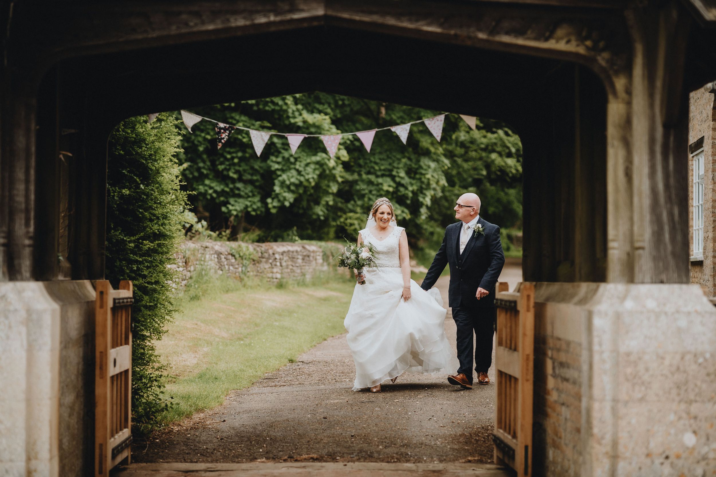 A couple stands in a covered archway entrance decorated with bunting flags on their countryside wedding day.
