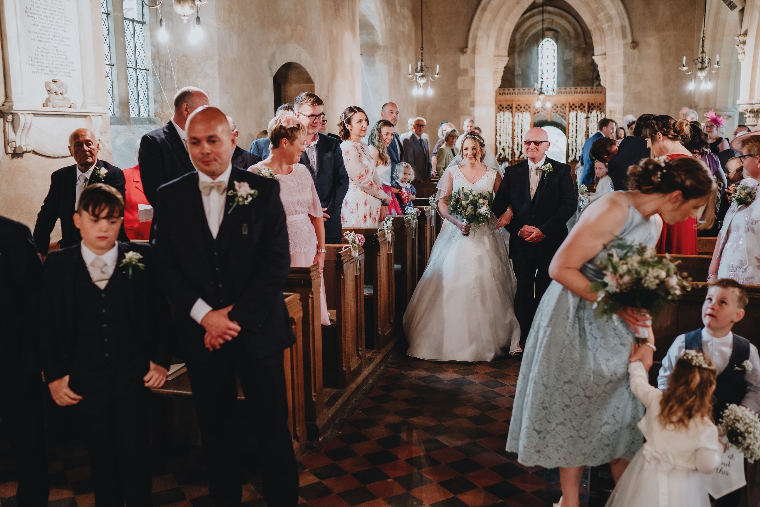 Wedding guests and ceremony participants stand together in a historic church with stone walls and ornate architecture.
