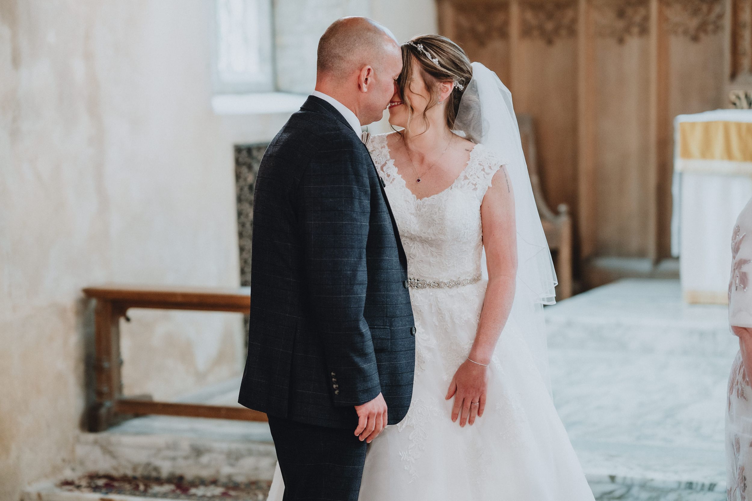 A romantic wedding moment captured in a rustic stone church interior with soft natural lighting.