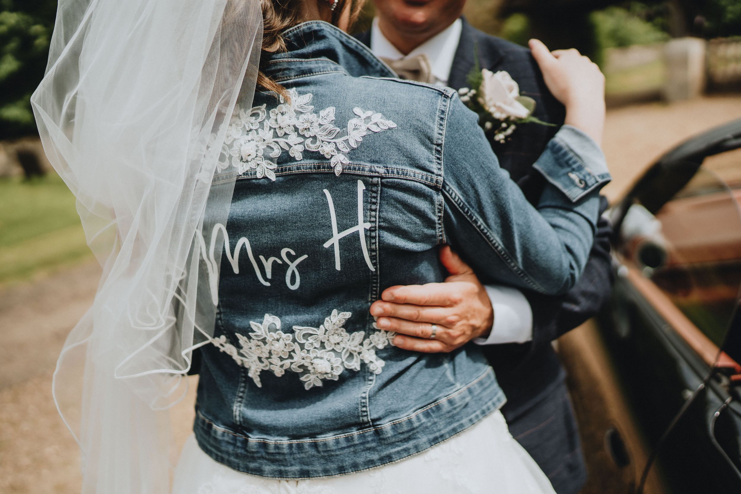 Custom denim jacket with embroidered wedding text worn over white dress.