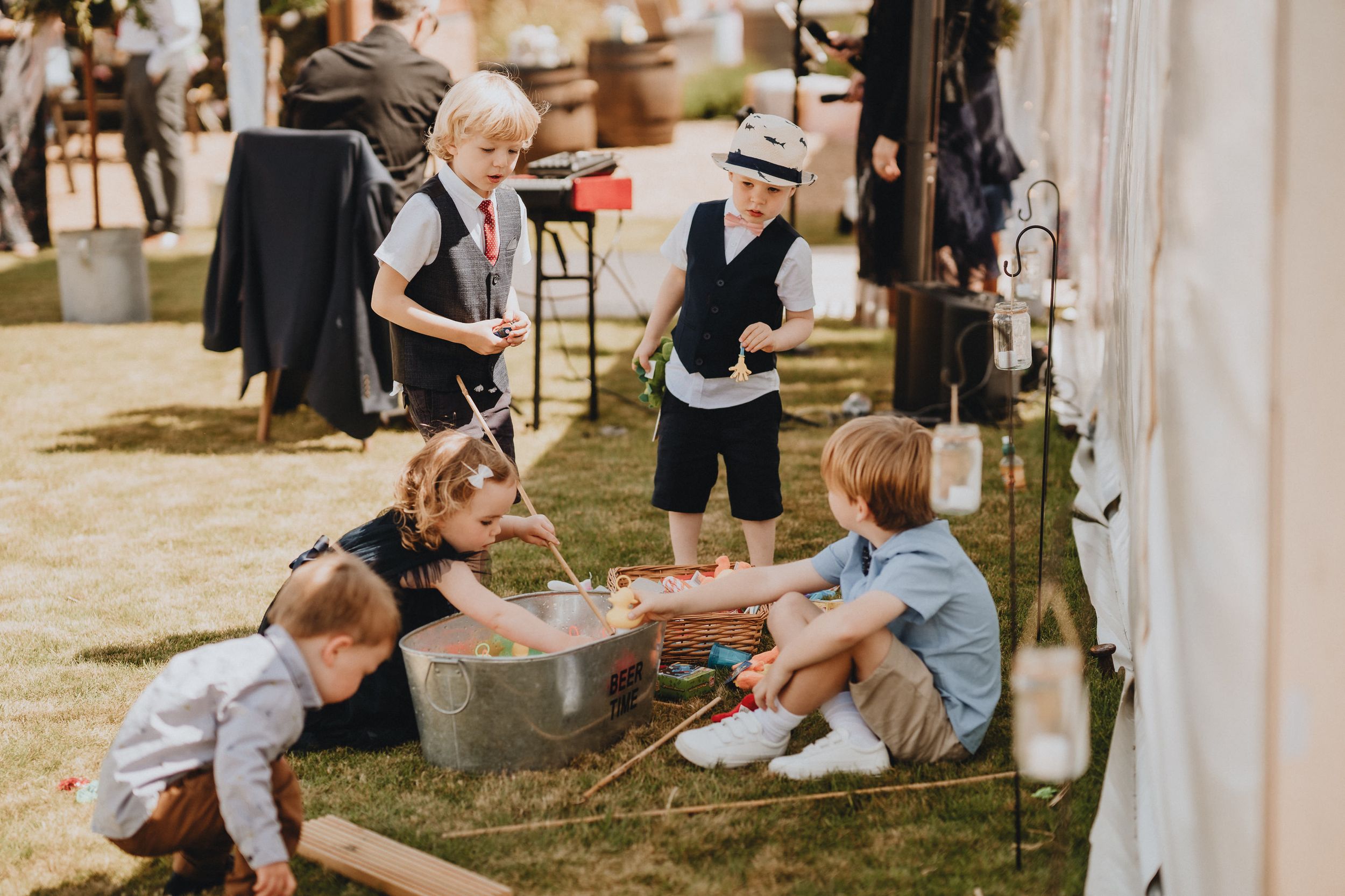 Children and adults gathered at an outdoor event playing games on the grass near clothing displays.