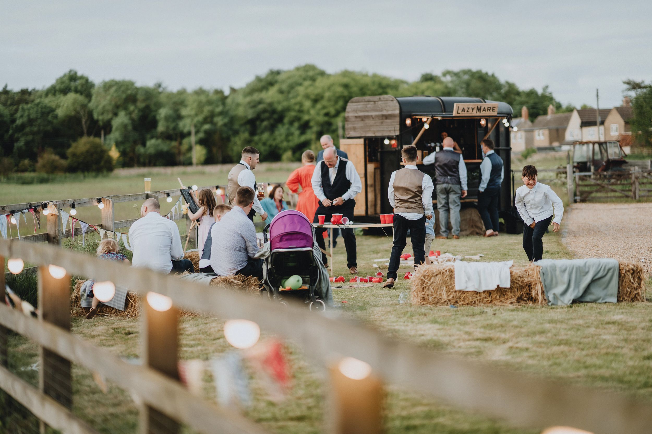Outdoor gathering in a field with guests, musical instruments, and string lights setup for an event.