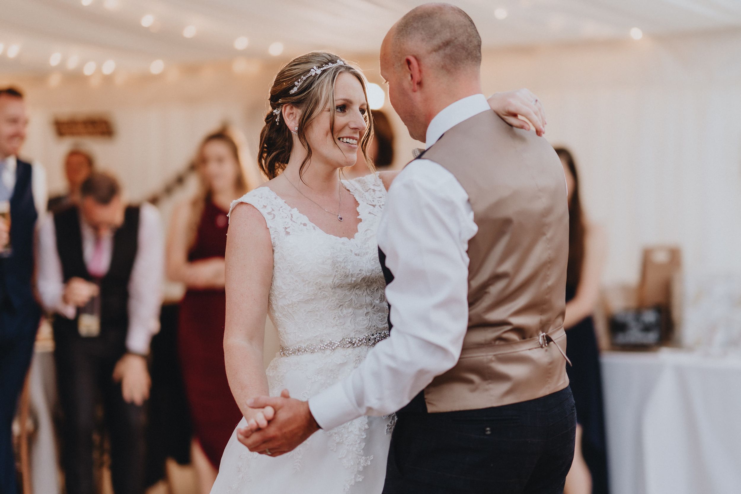 Two people share a tender moment during their first dance at a wedding reception in a light-filled indoor venue.