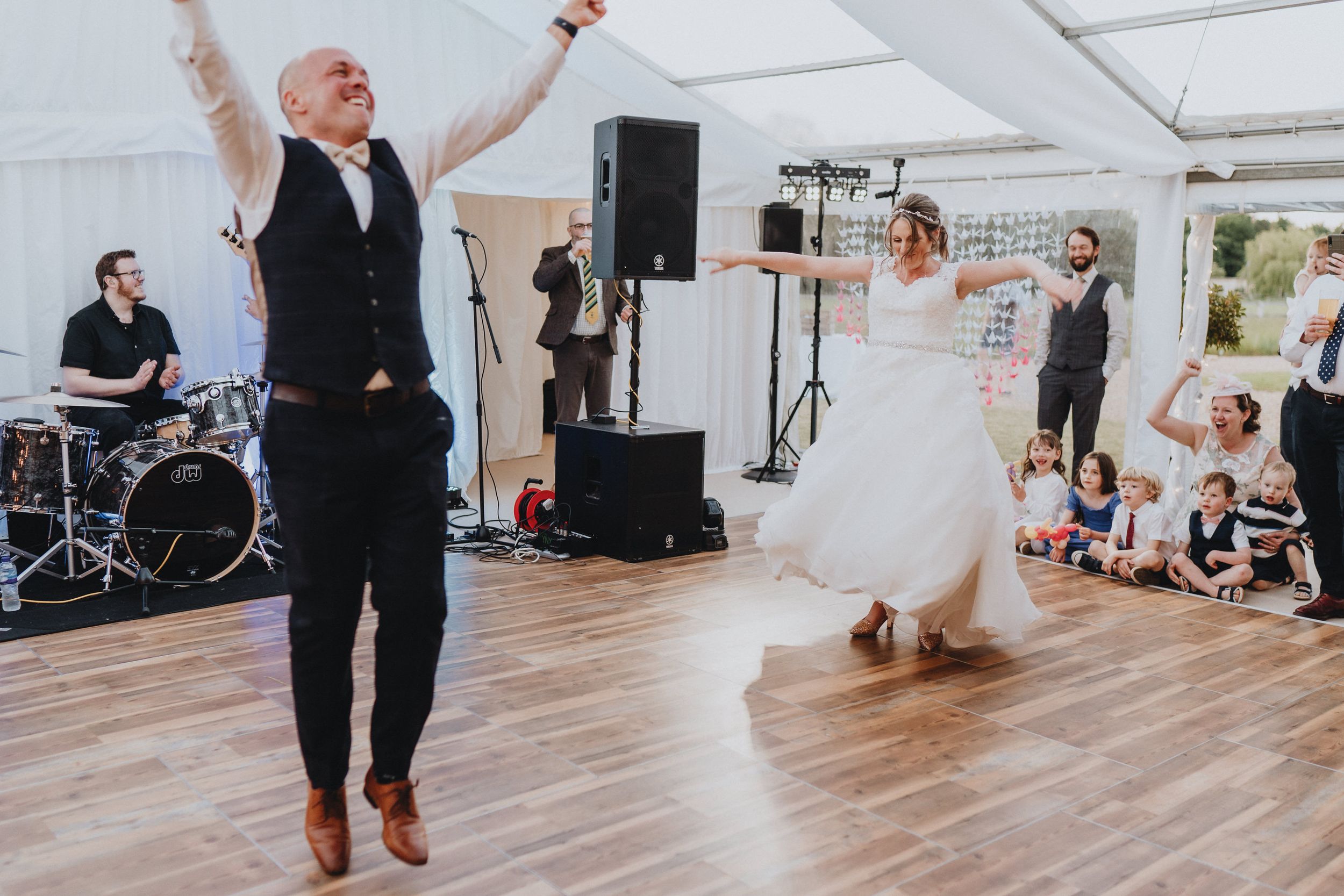 Wedding guests dancing with joyful energy on a wooden dance floor inside a white tent reception venue.