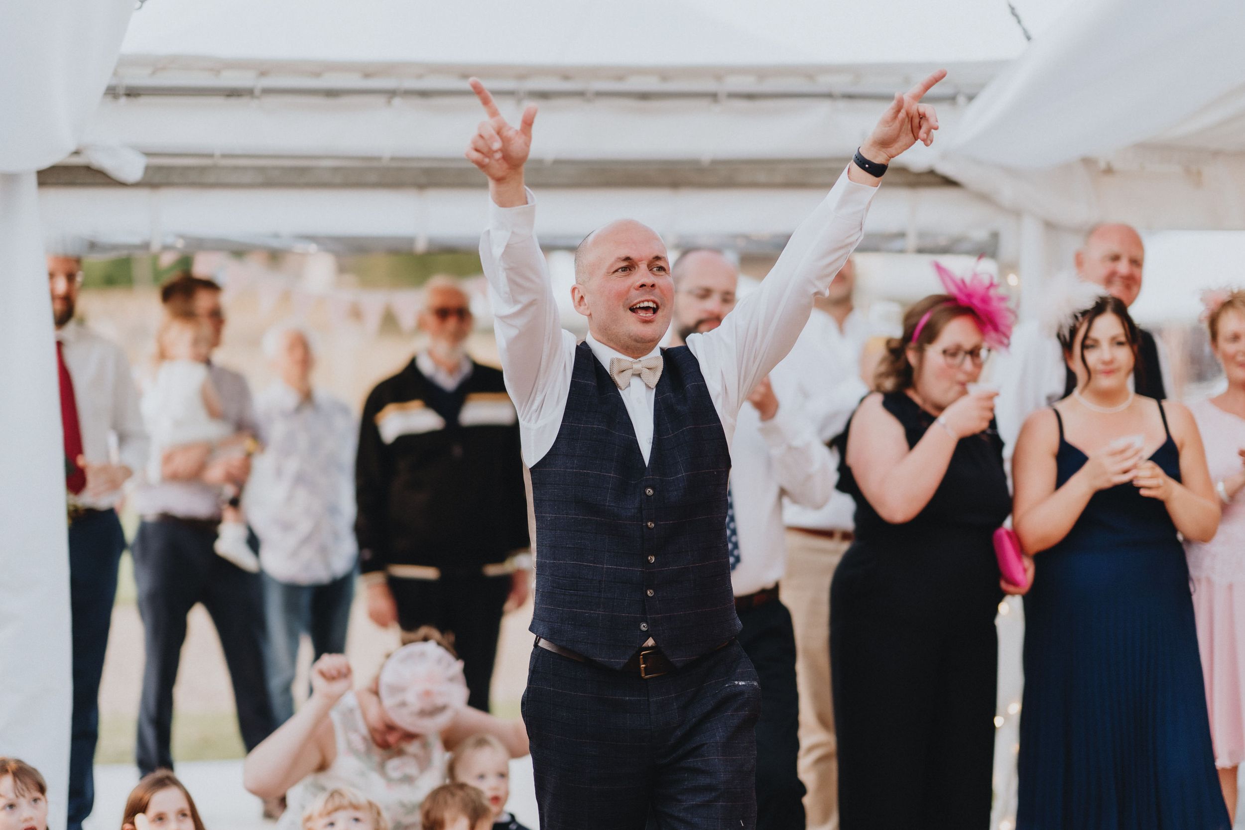 Party guests dance and celebrate with joy at an indoor event as someone raises their hands in celebration.