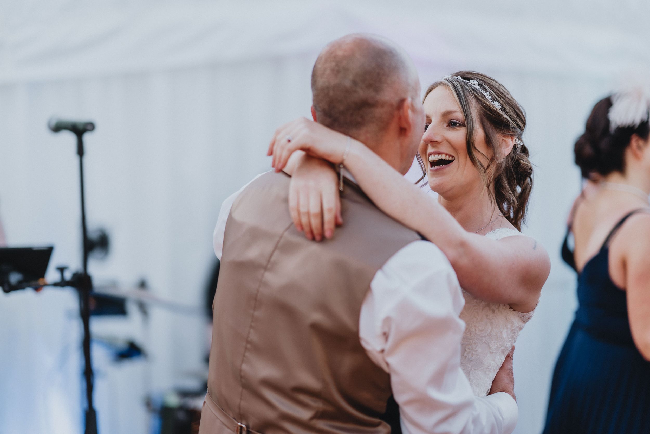 Newlyweds share a joyful dance moment under white tent lighting at their wedding reception.