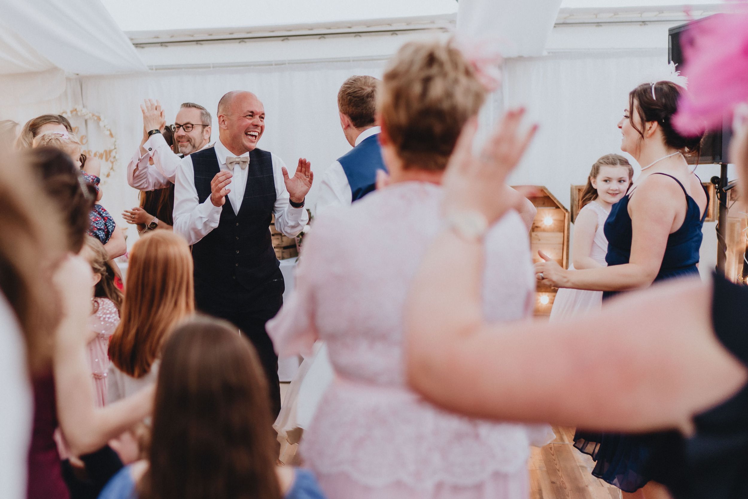 A lively dance floor filled with guests celebrating at a wedding reception in a bright indoor venue.