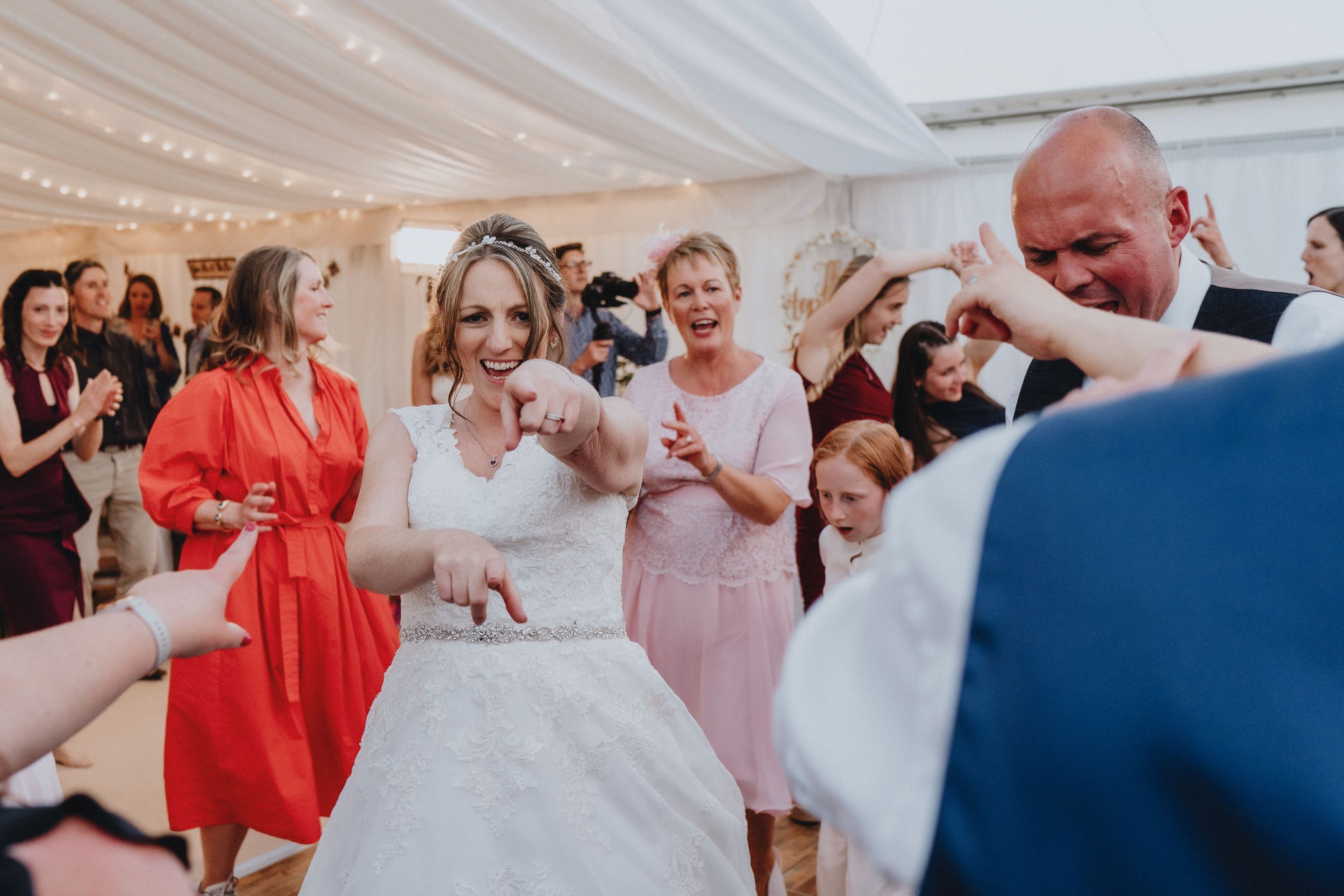 Wedding guests celebrate on the dance floor as a bride in white dress dances surrounded by loved ones.