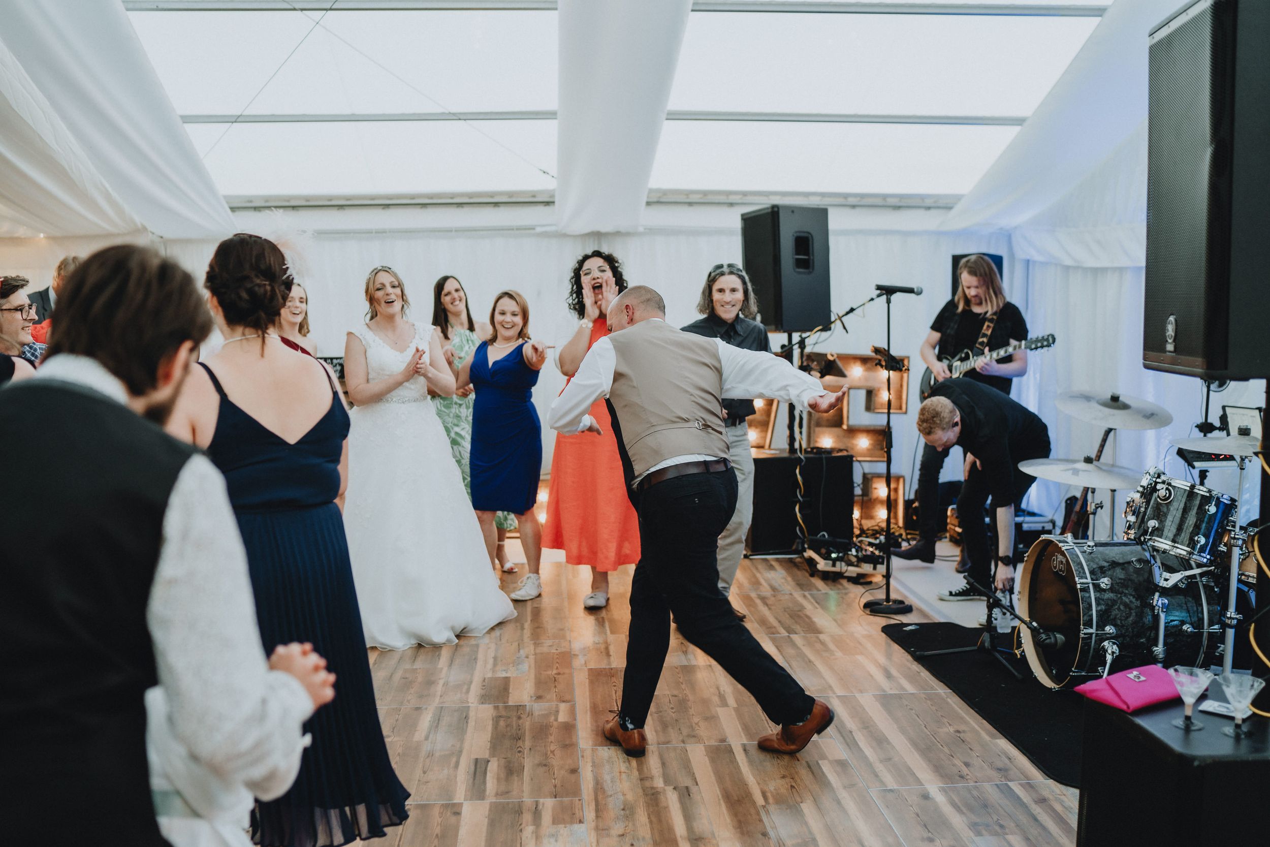 People dancing at a wedding reception on a wooden dance floor near a live band setup.