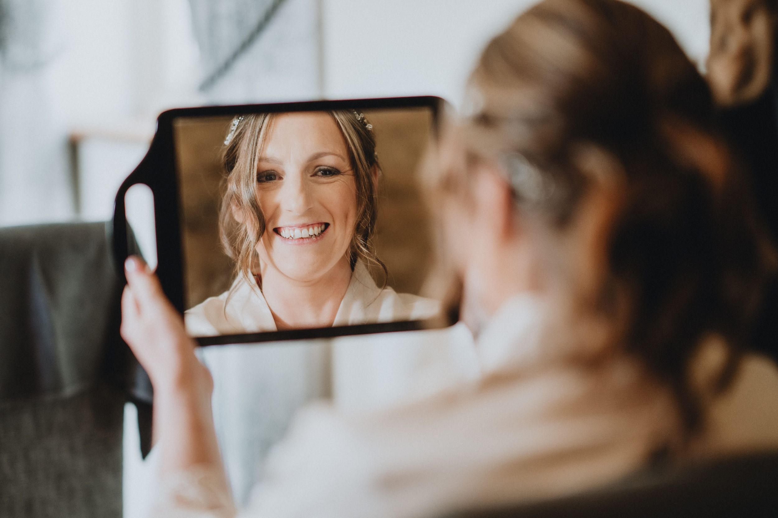 Someone holding a tablet displaying a video call with a smiling person in white clothing against a light background.