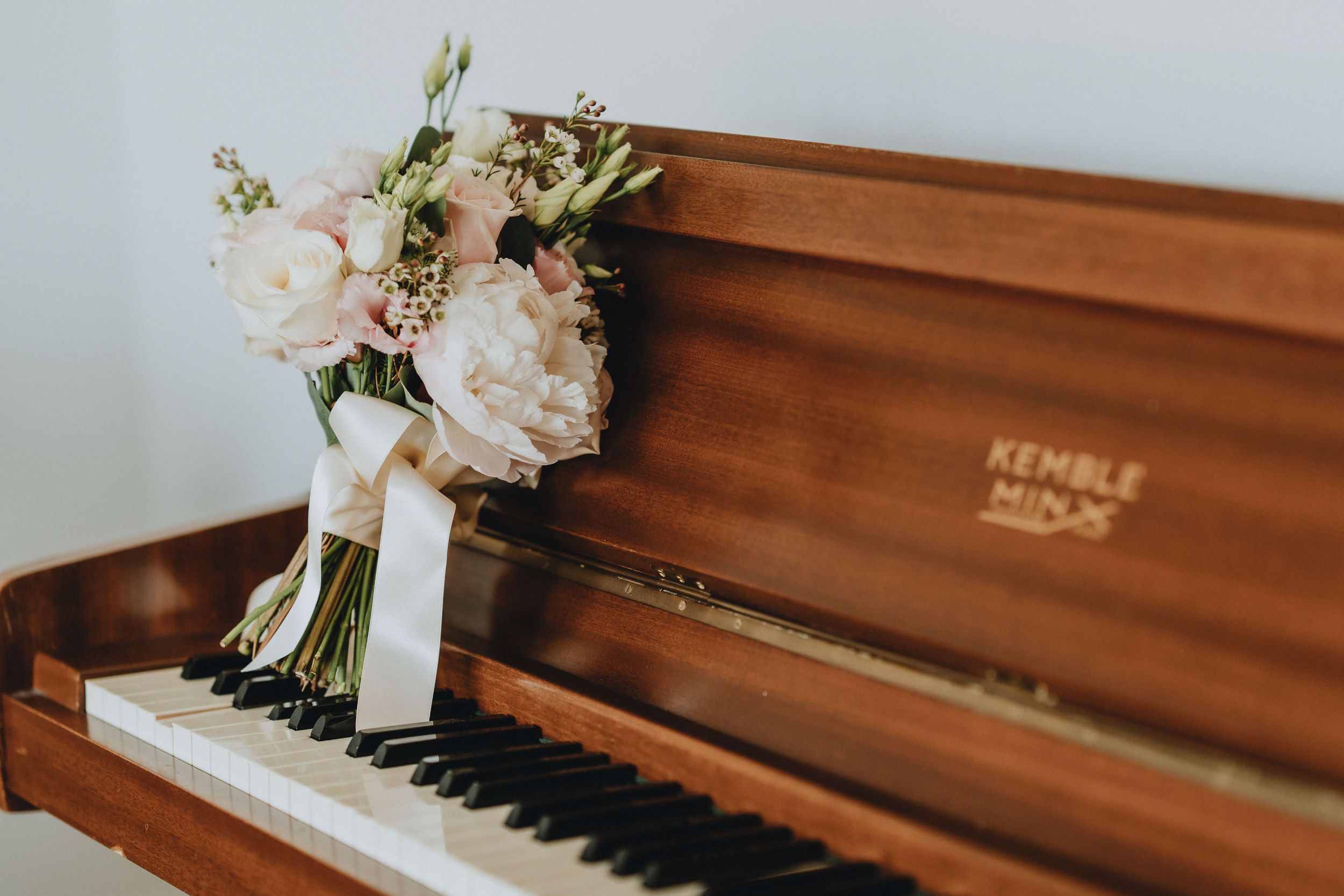 A bouquet of blush pink roses and greenery rests atop a wooden Kendle piano keyboard.