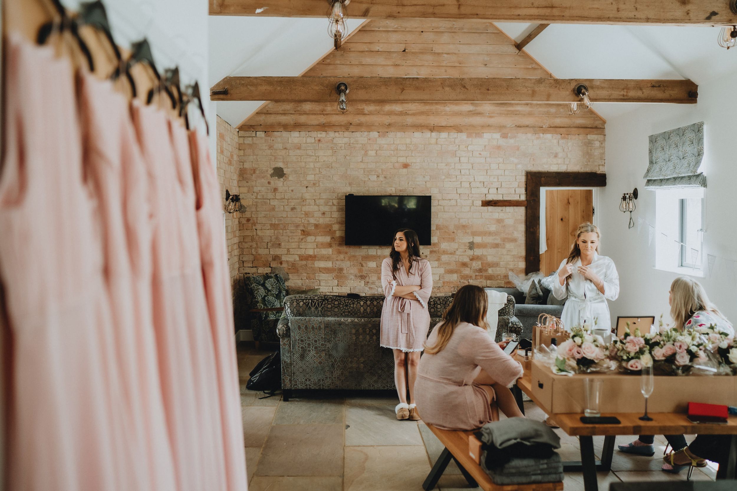 Wedding party getting ready in rustic barn venue with exposed wooden beams and blush pink decor details.