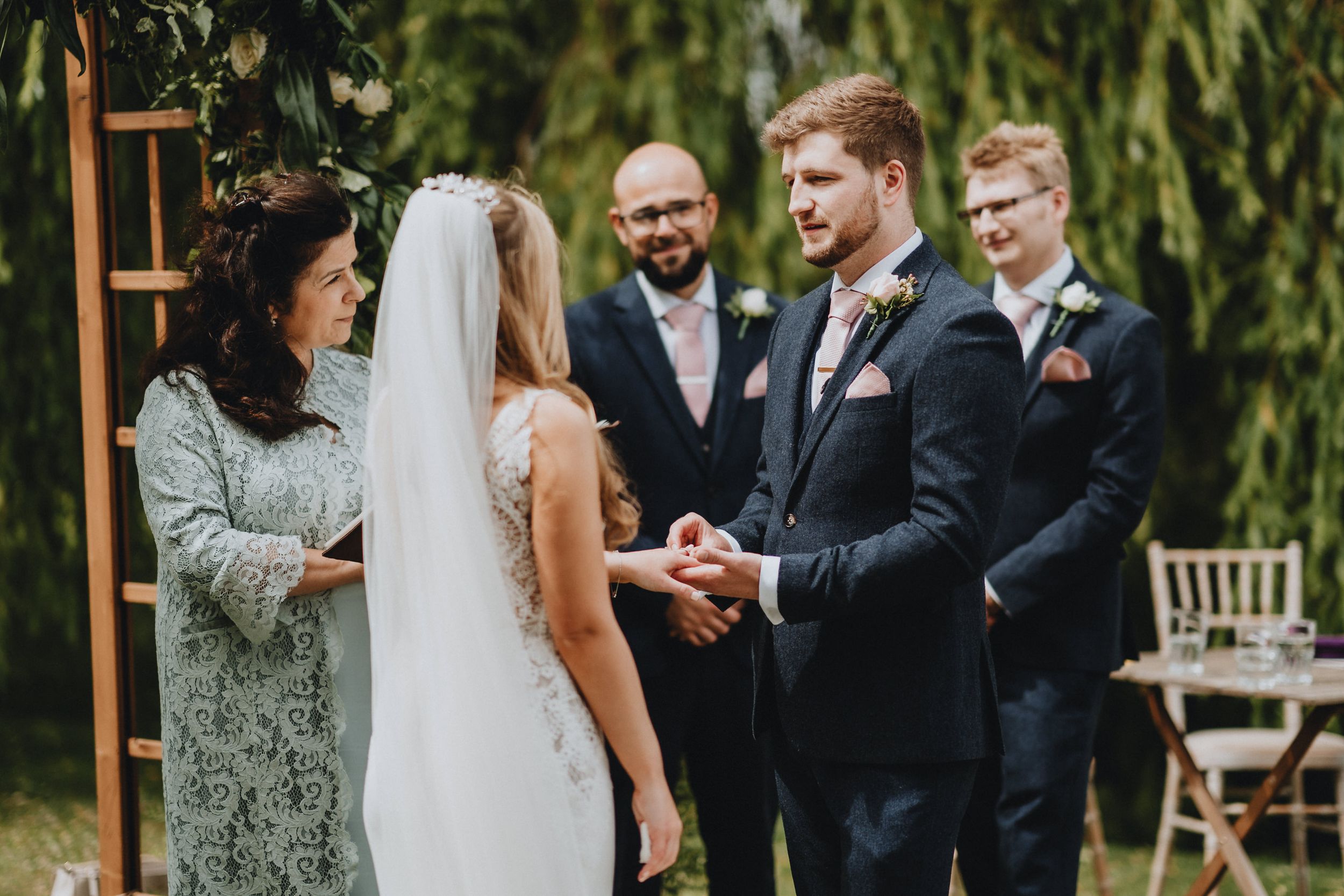An outdoor wedding ceremony taking place under a willow tree with formal attire and decorations.