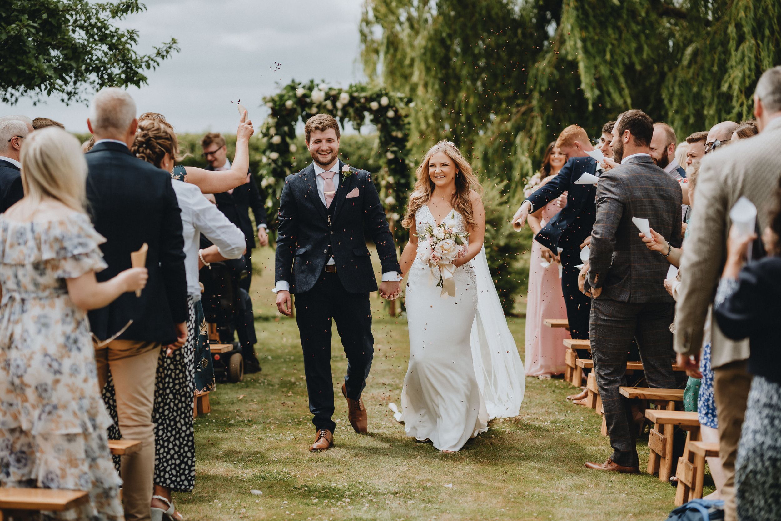 A joyful outdoor wedding ceremony with guests lining the aisle as a couple walks through on their special day.