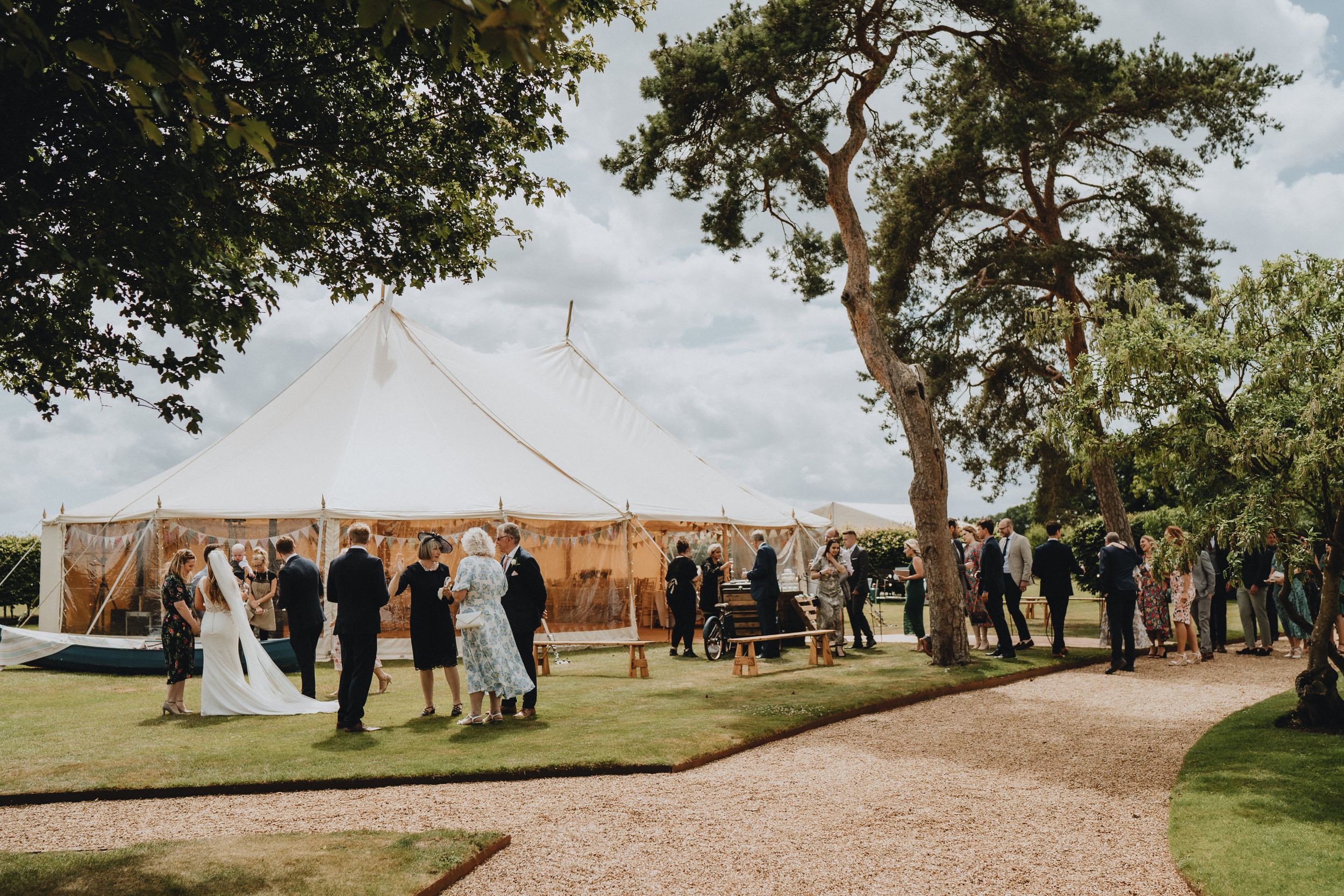 A white tent wedding reception at Lattenbury Hill setup on a lawn with guests mingling outdoors on a sunny day.