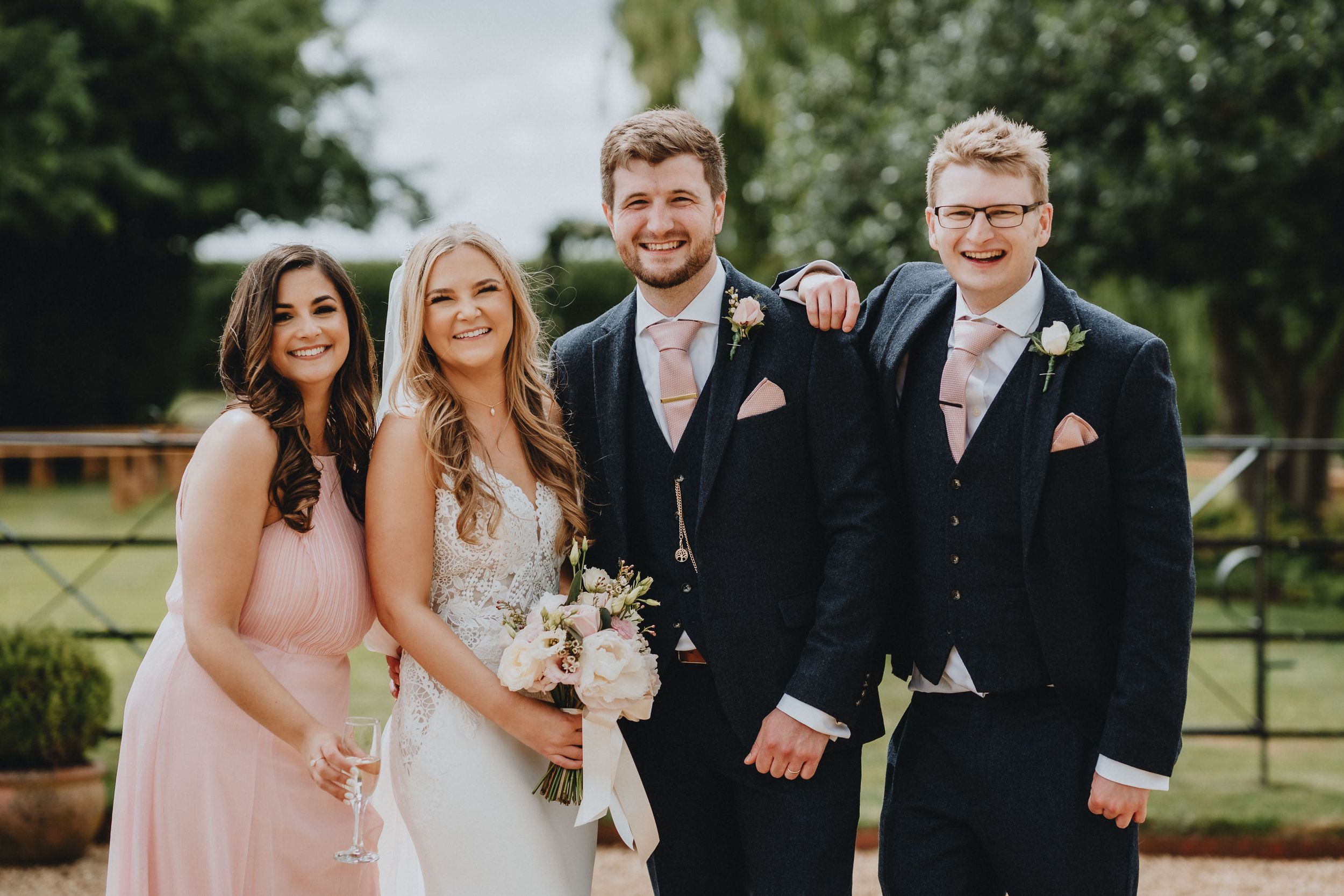 Wedding party members in formal attire pose together outdoors during a spring celebration.