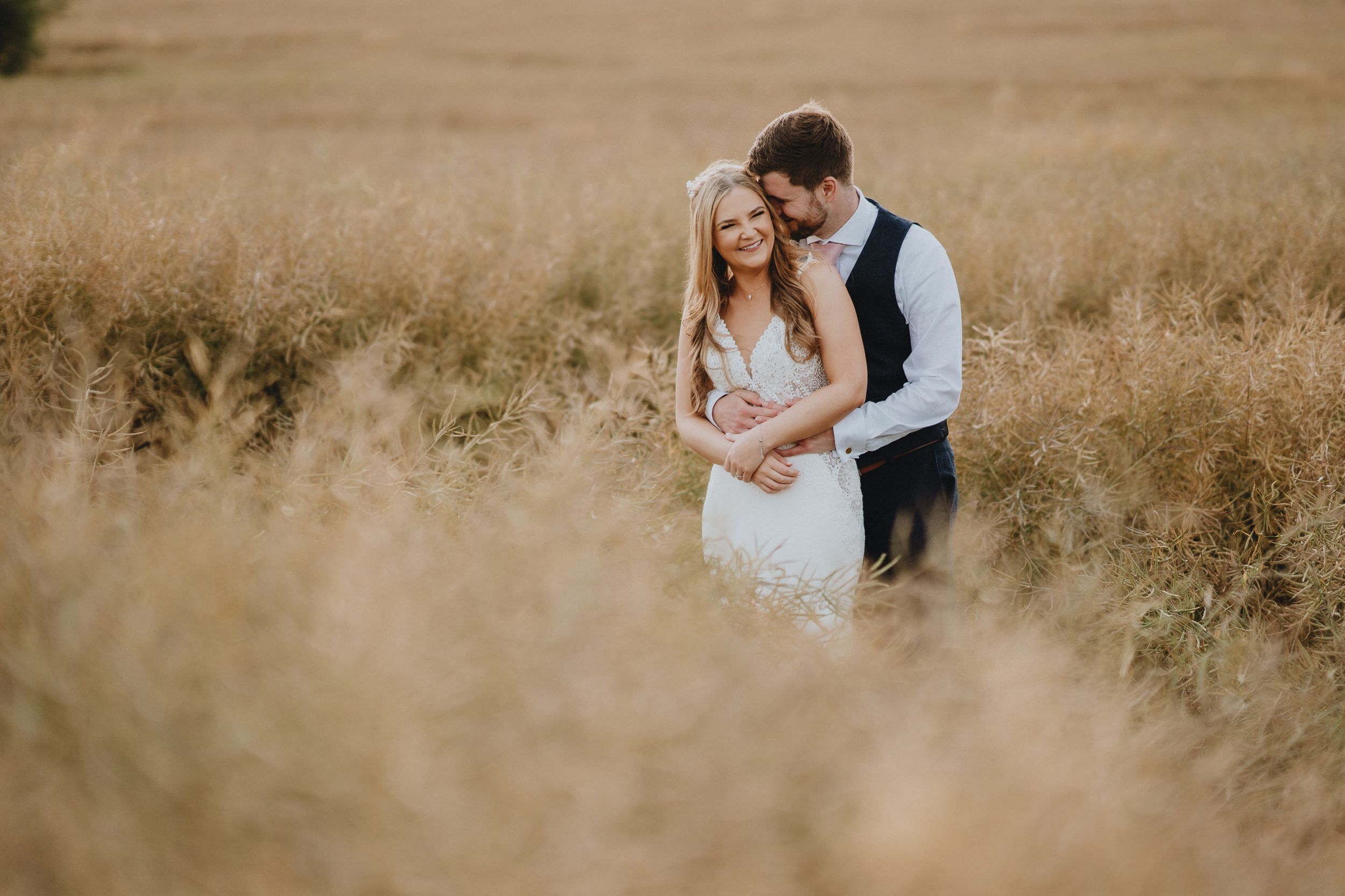 A romantic wedding couple embraces in a golden wheat field during sunset.