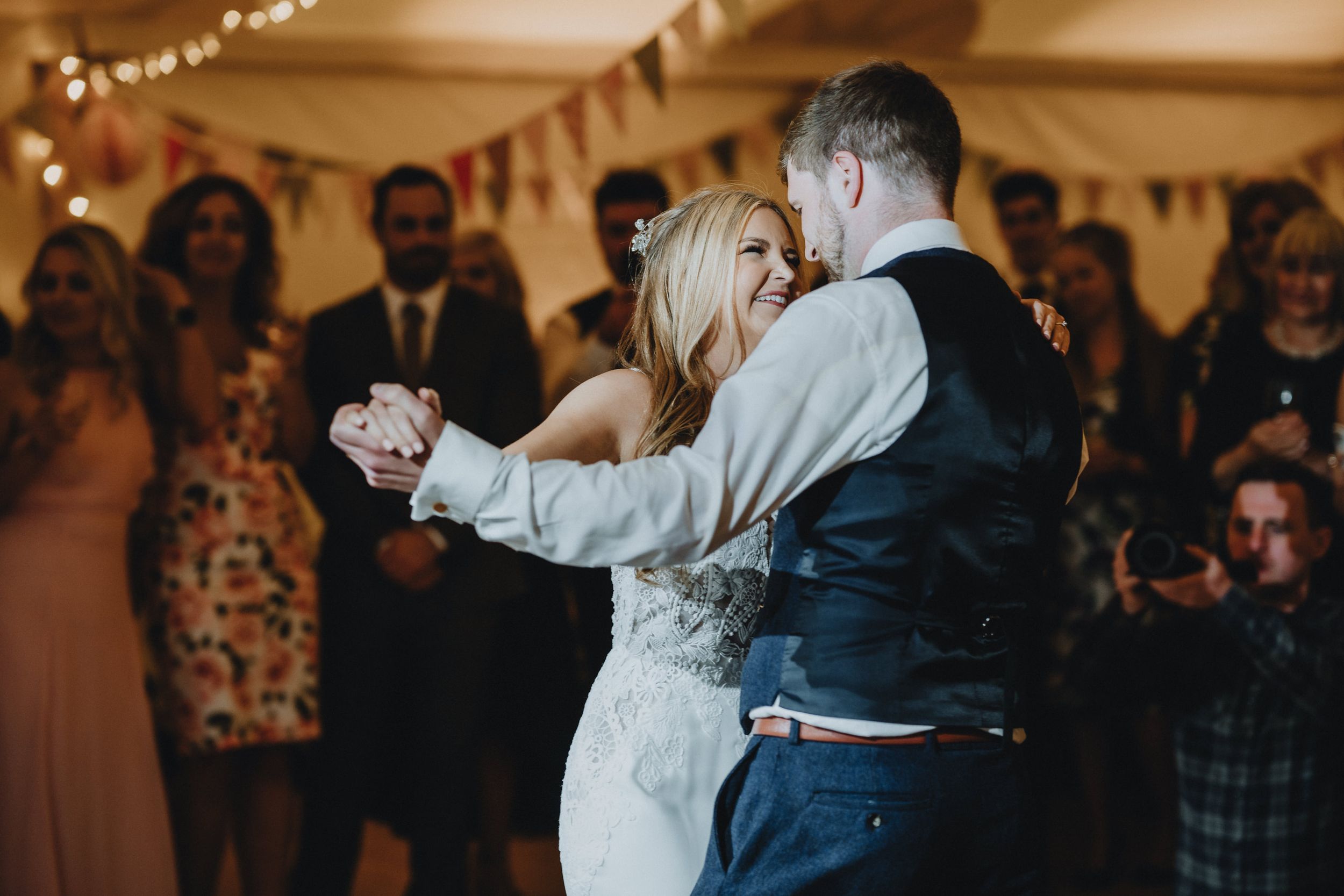 A couple sharing their first dance at a wedding reception under twinkling lights with guests watching.