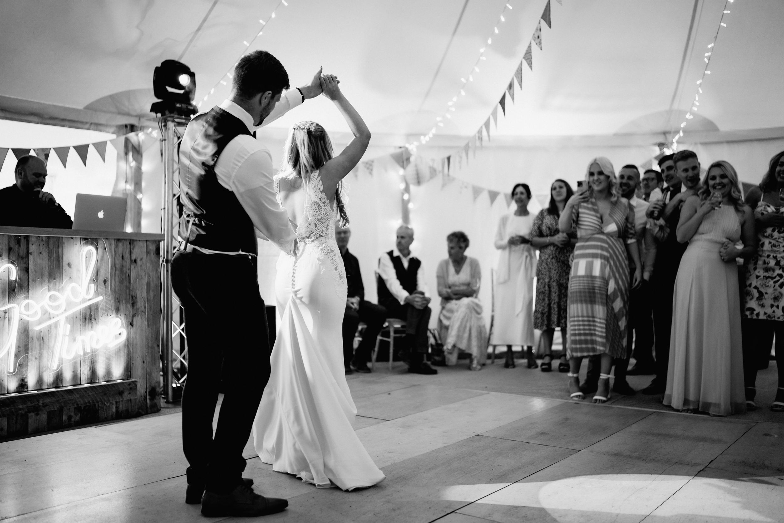 A romantic first dance moment in black and white at a wedding reception under a tent with guests watching.