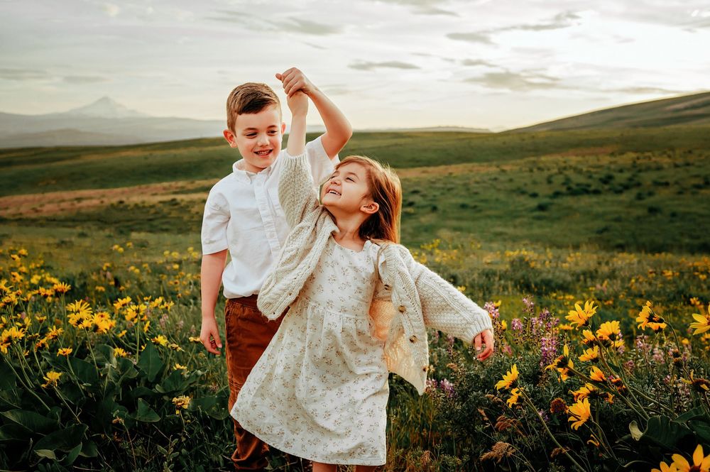 Children playing and dancing together in field of yellow wildflowers at sunset.