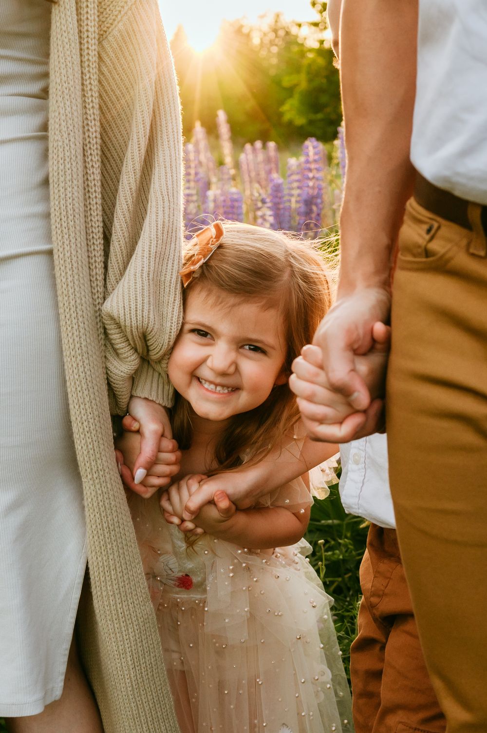 Smiling child holding parents' hands between them in lavender field at sunset.