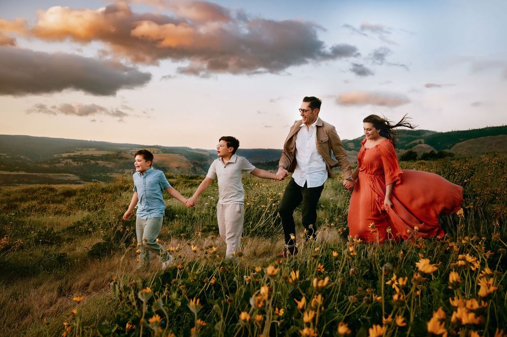 Group walking hand in hand through wildflower field at sunset with mountains in background.