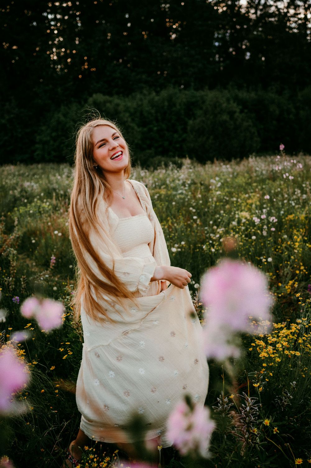 Woman in white dress laughing joyfully in wildflower meadow at dusk.