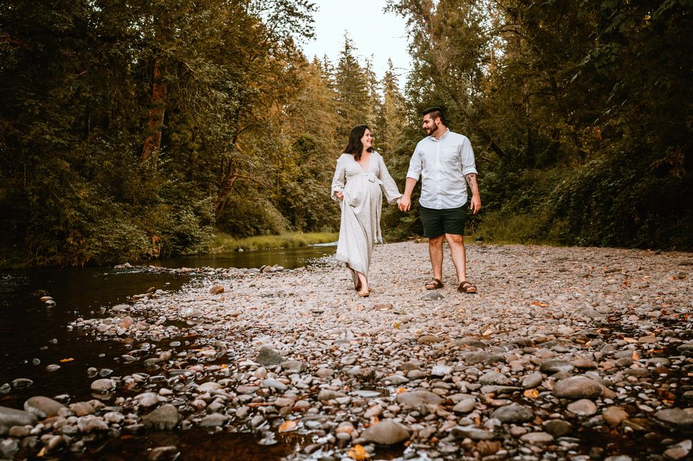 Couple walking together on rocky riverbed path through forest.