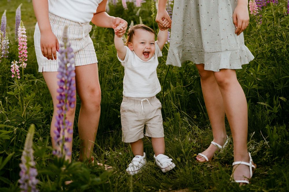 A toddler jumps with joy among blooming lupines in a garden.