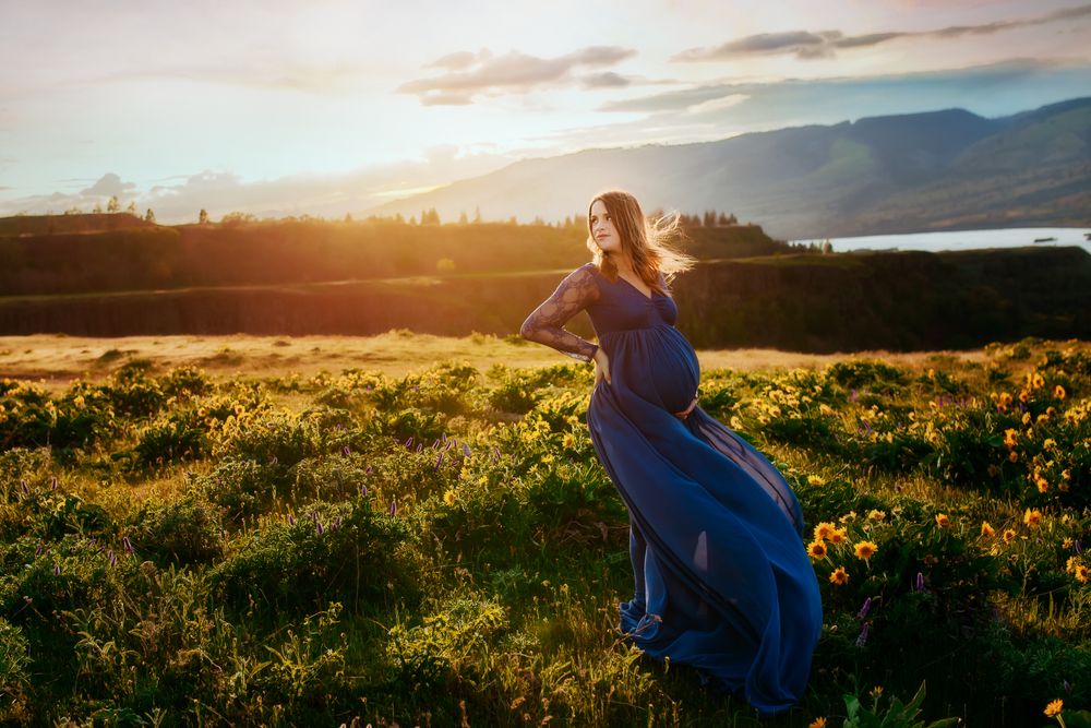 A flowing blue dress catches the golden sunset light in a wildflower meadow with mountains in the background.