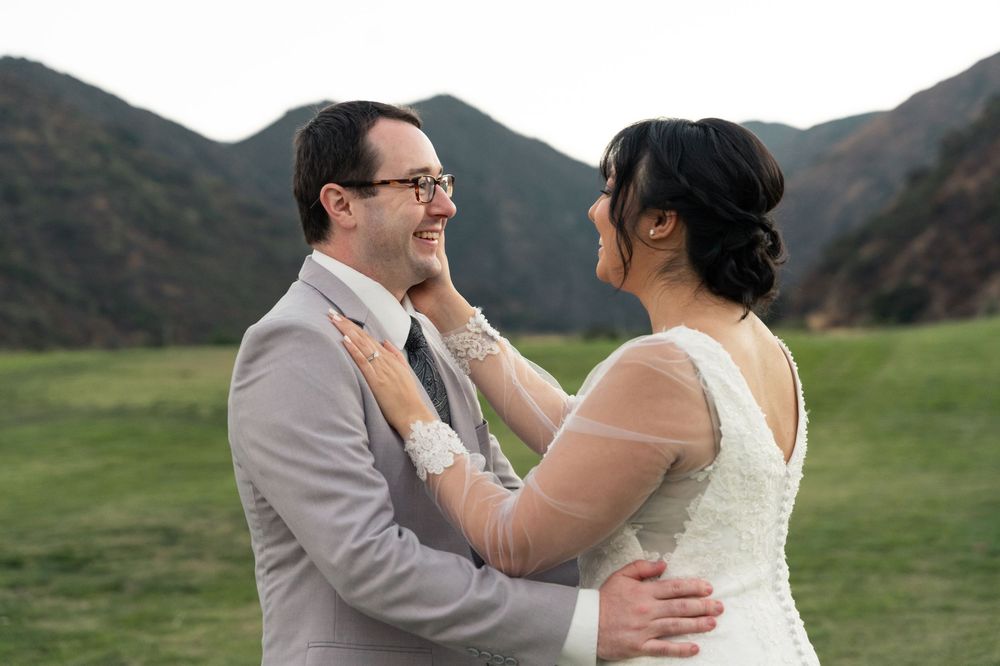 A bride and groom share an intimate moment together in a mountain meadow, surrounded by rolling hills at sunset.