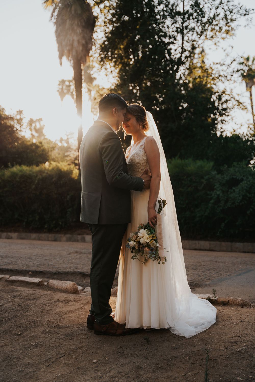 A romantic sunset wedding photo shows a couple embracing on a dirt path with palm trees and golden light in the background.