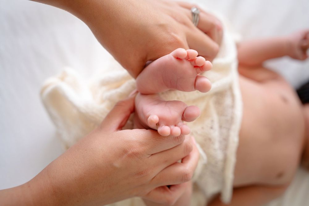 Gentle hands massaging tiny baby feet wrapped in soft white fabric.