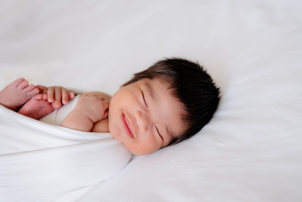 Peaceful sleeping newborn baby wrapped in white blanket on light background.