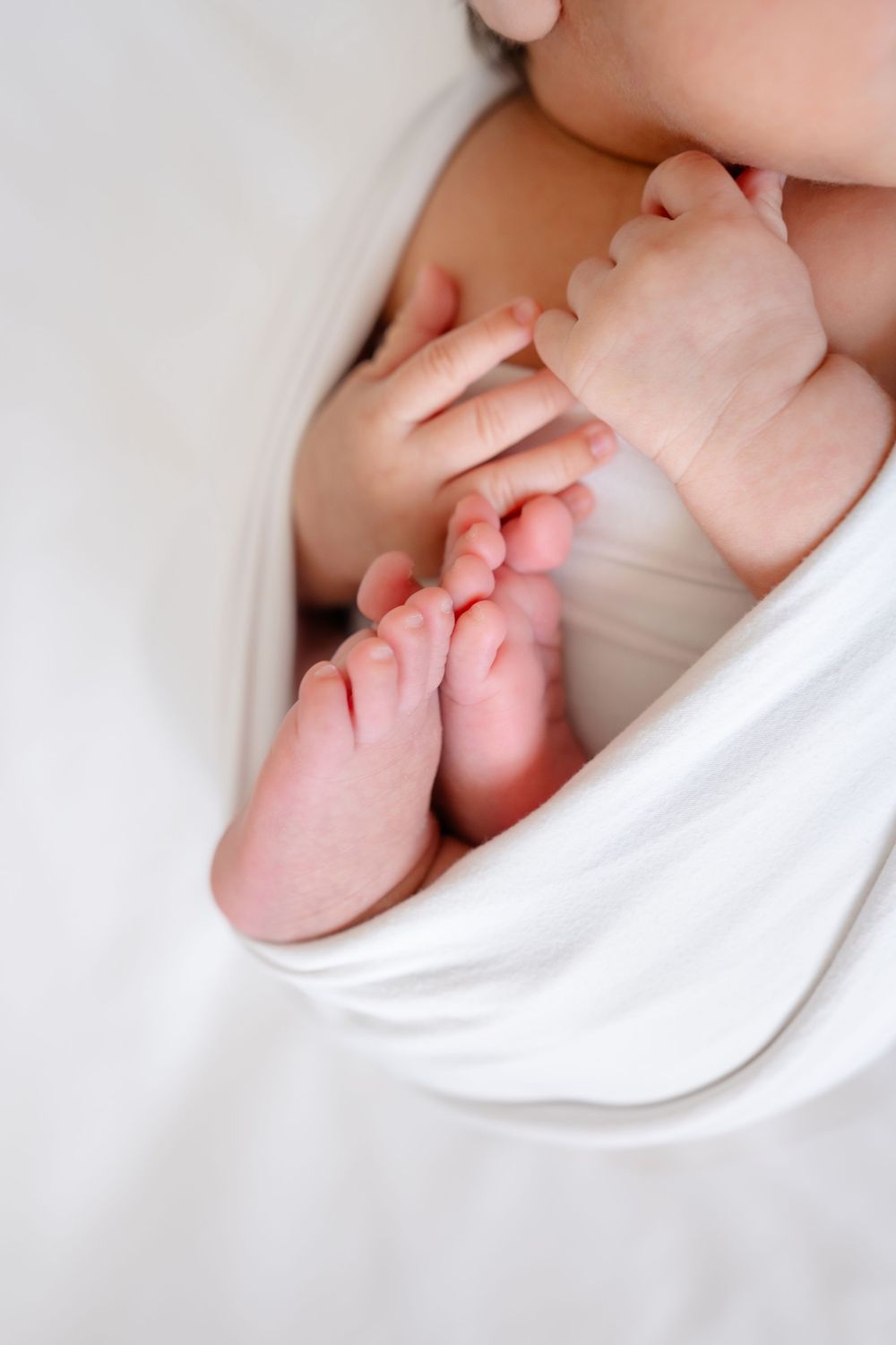 Close-up of tiny baby feet and hands wrapped in soft white fabric.