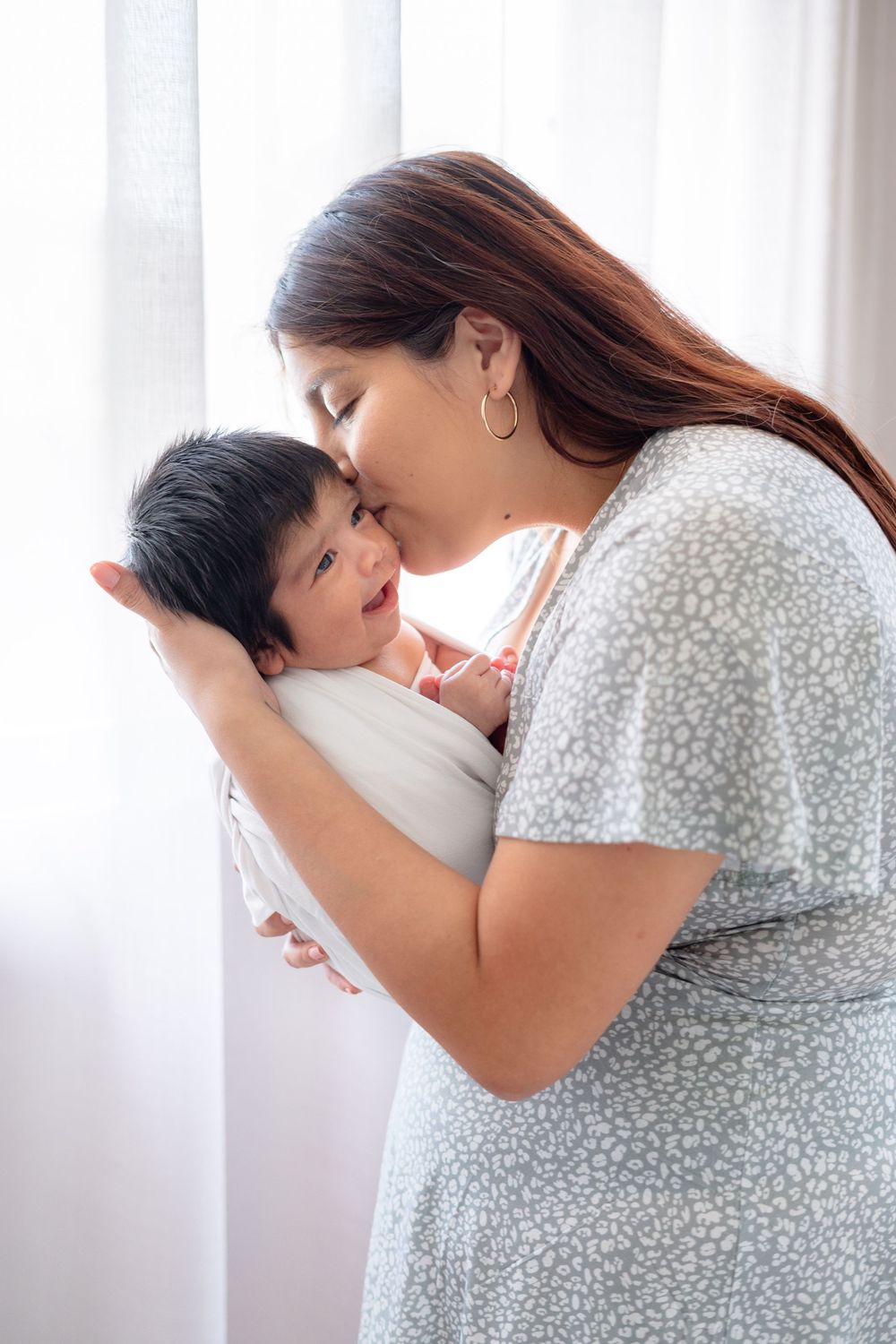 A tender moment between parent and child by a bright window with white curtains.