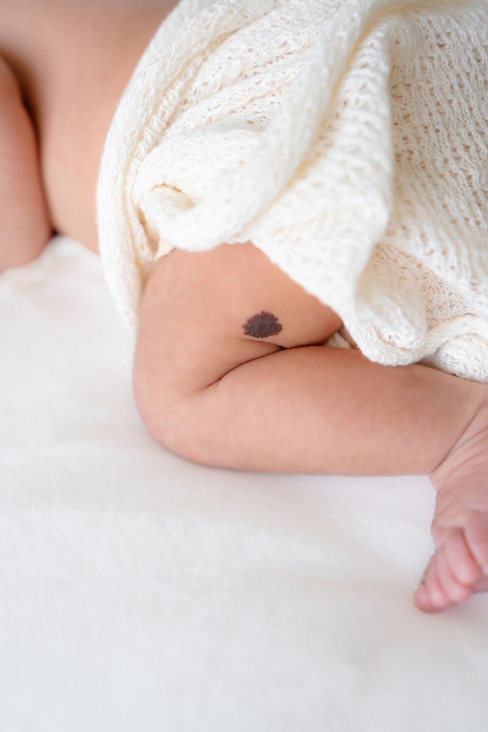 Close-up of a small heart-shaped tattoo on skin with white knit fabric.