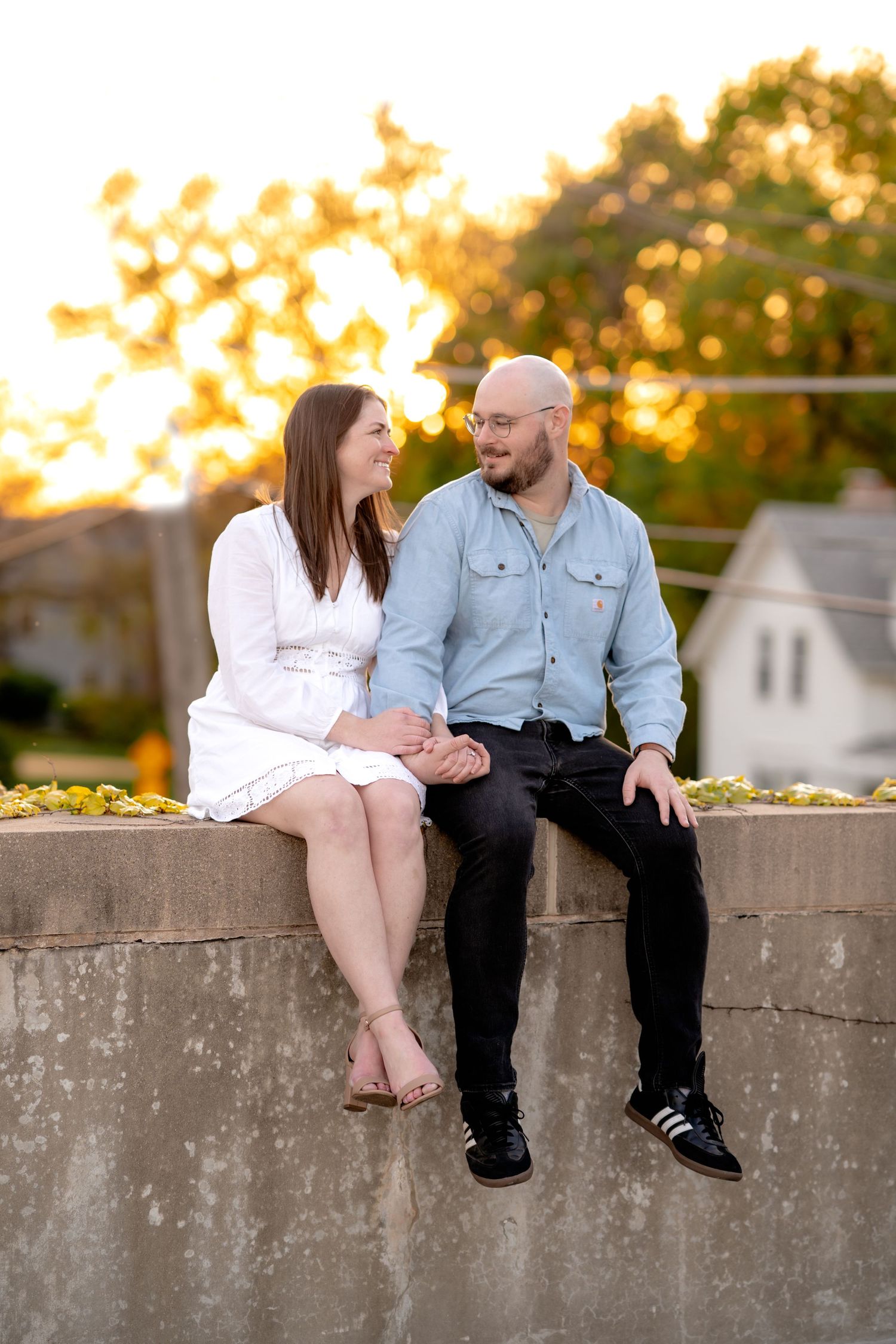 A couple sits together on a concrete wall at sunset, sharing an intimate moment in warm evening light.