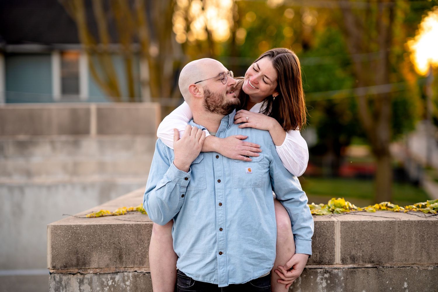 A joyful couple shares a playful piggyback moment at sunset in an outdoor setting with warm golden lighting.