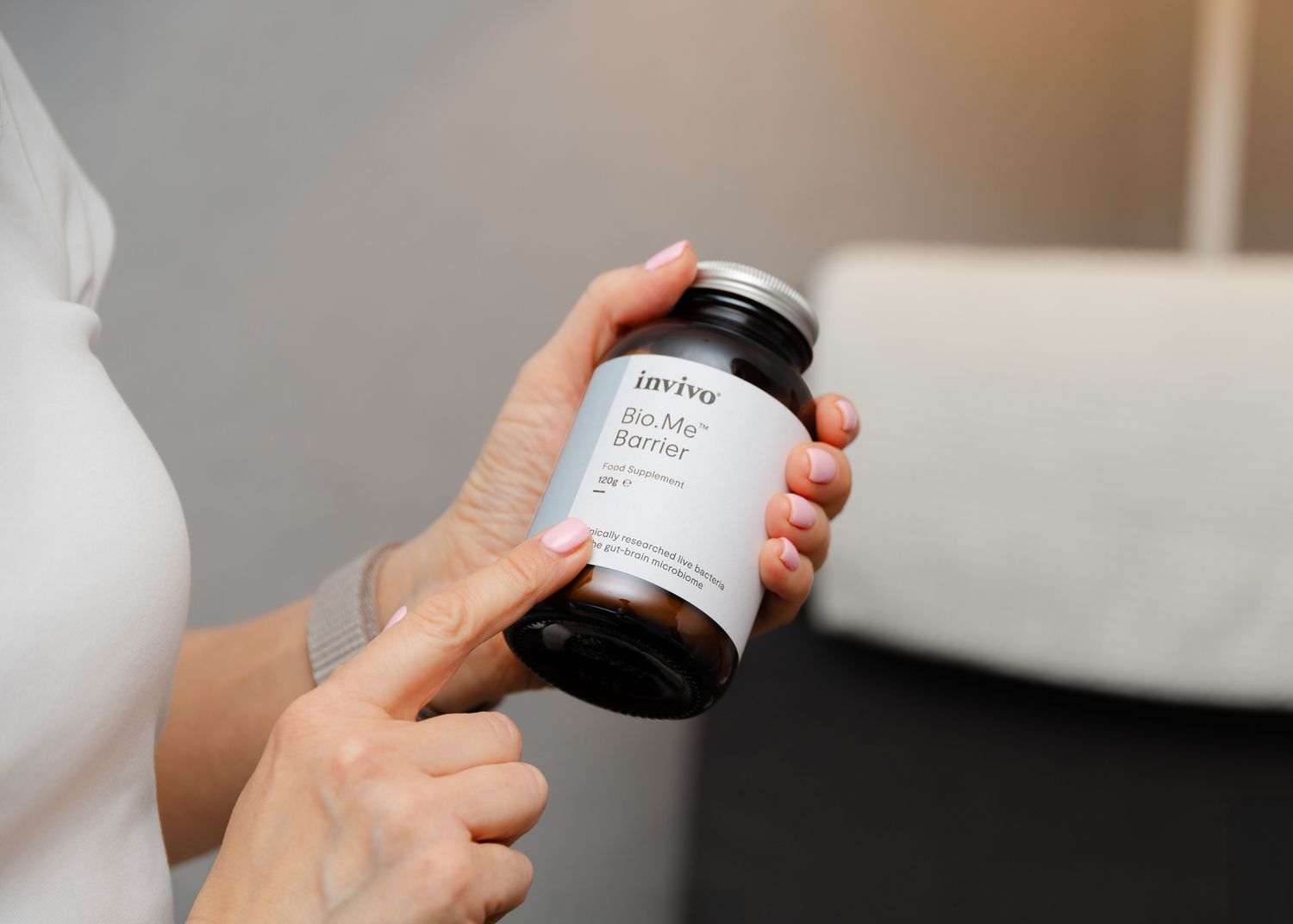 Hands holding a black glass bottle with a minimalist product label against a blurred neutral background.