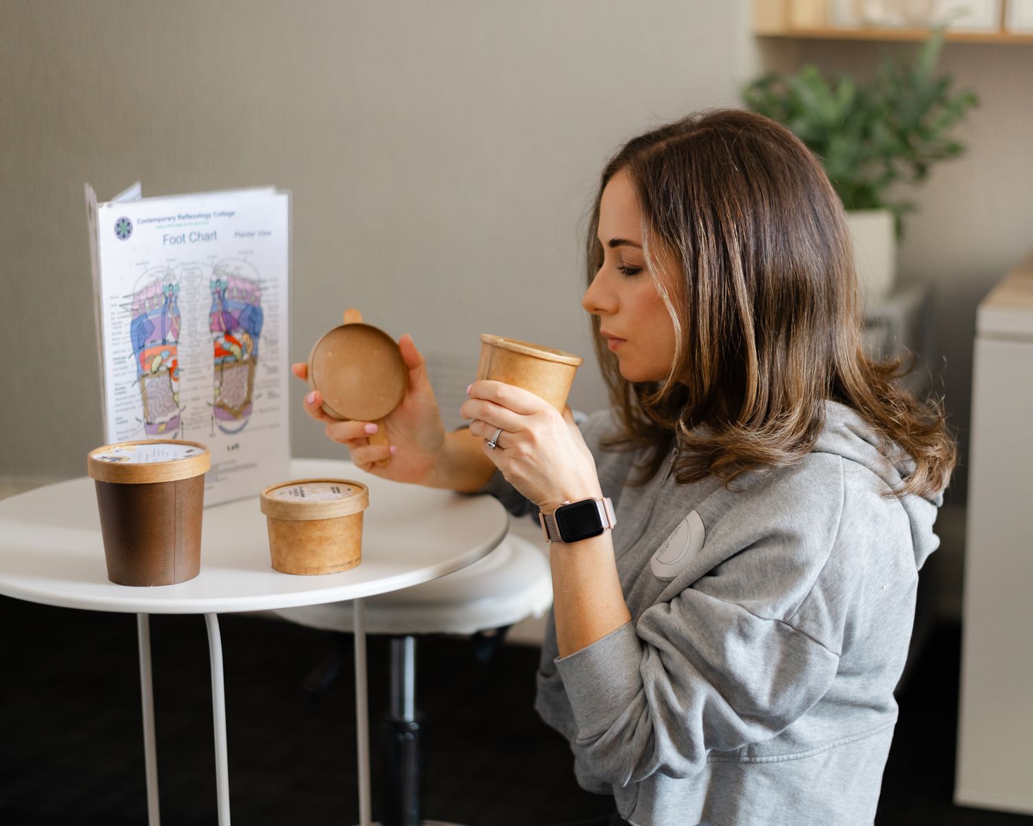 A person in a gray sweater enjoys coffee drinks at a cafe table with menu card displayed.