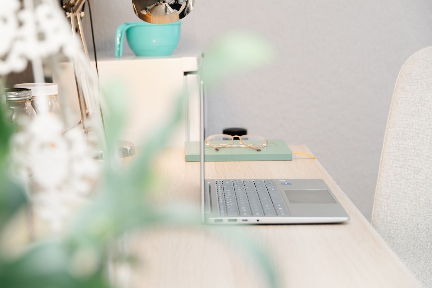 A minimalist white desk setup with a laptop, plants, and soft lighting creating a peaceful workspace atmosphere.